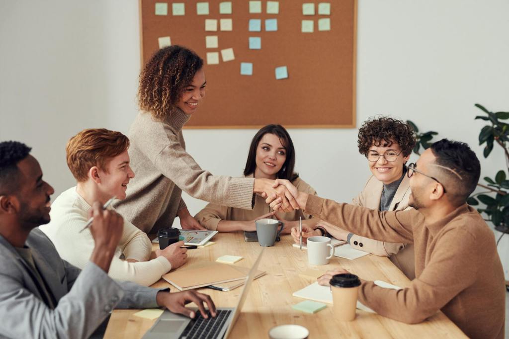 People sat around a table with two colleagues shaking hands