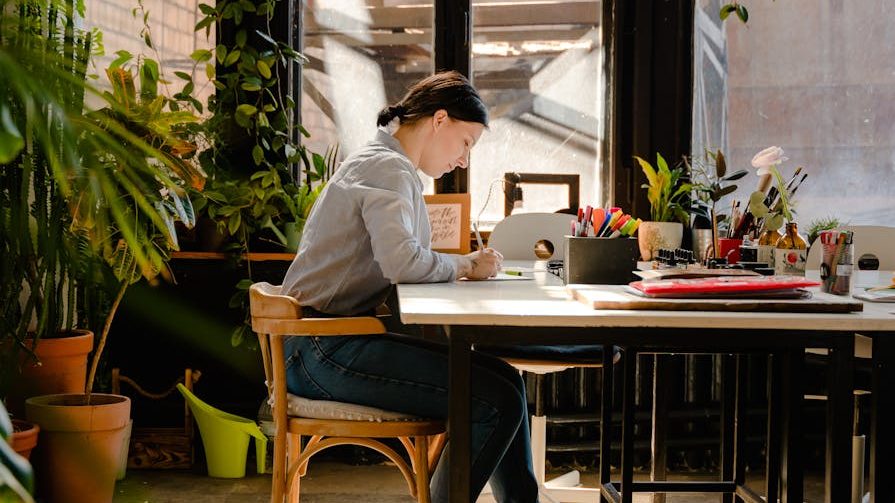 photo of woman sitting by the table while writing